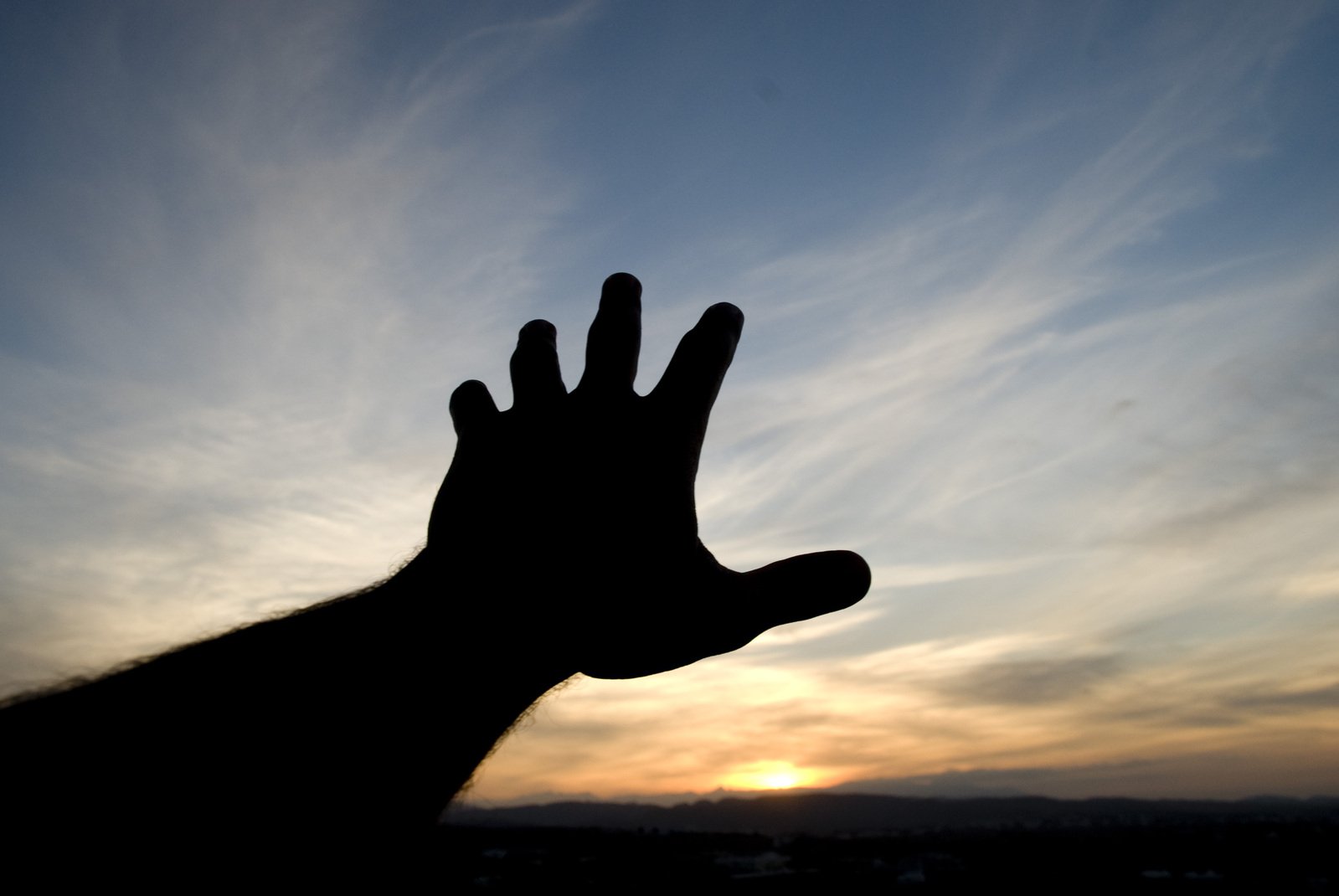 a silhouette shows the sunset and someone's hand in the air