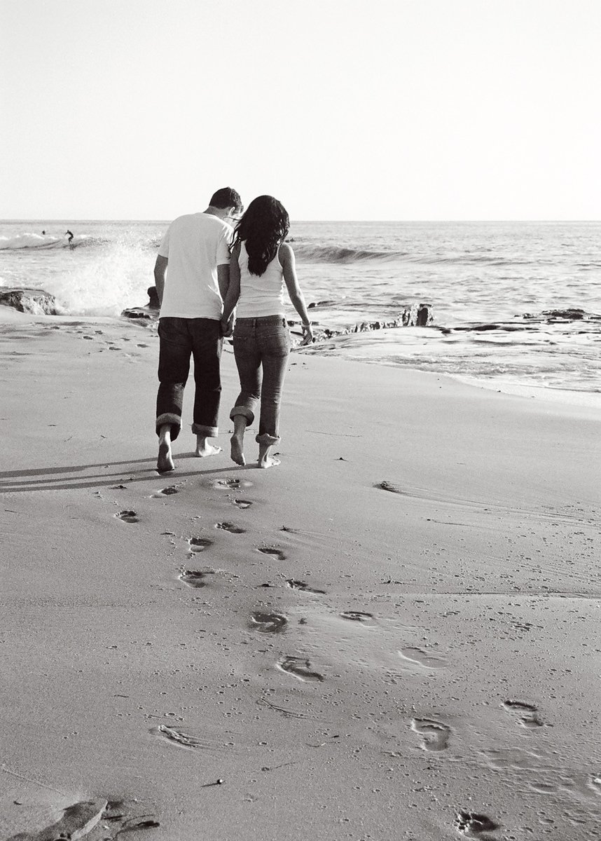 a man and a woman walk hand in hand along the beach