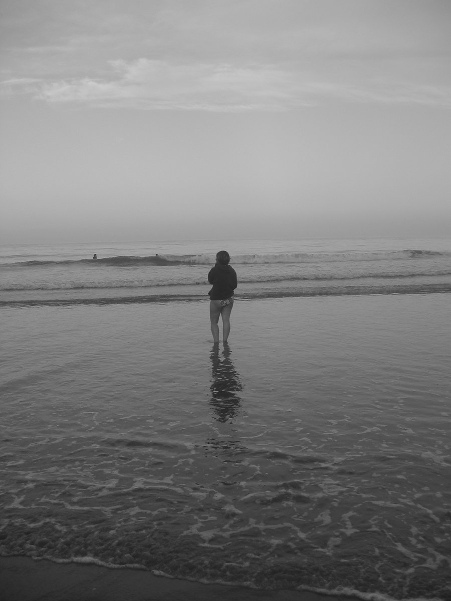 a person in black jacket standing on water at beach