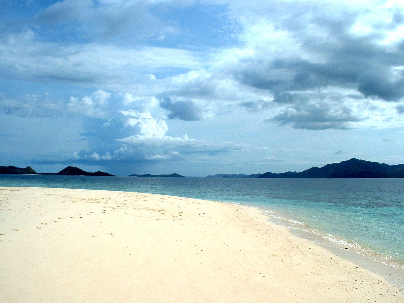 a wide open beach in the ocean with many small island in background