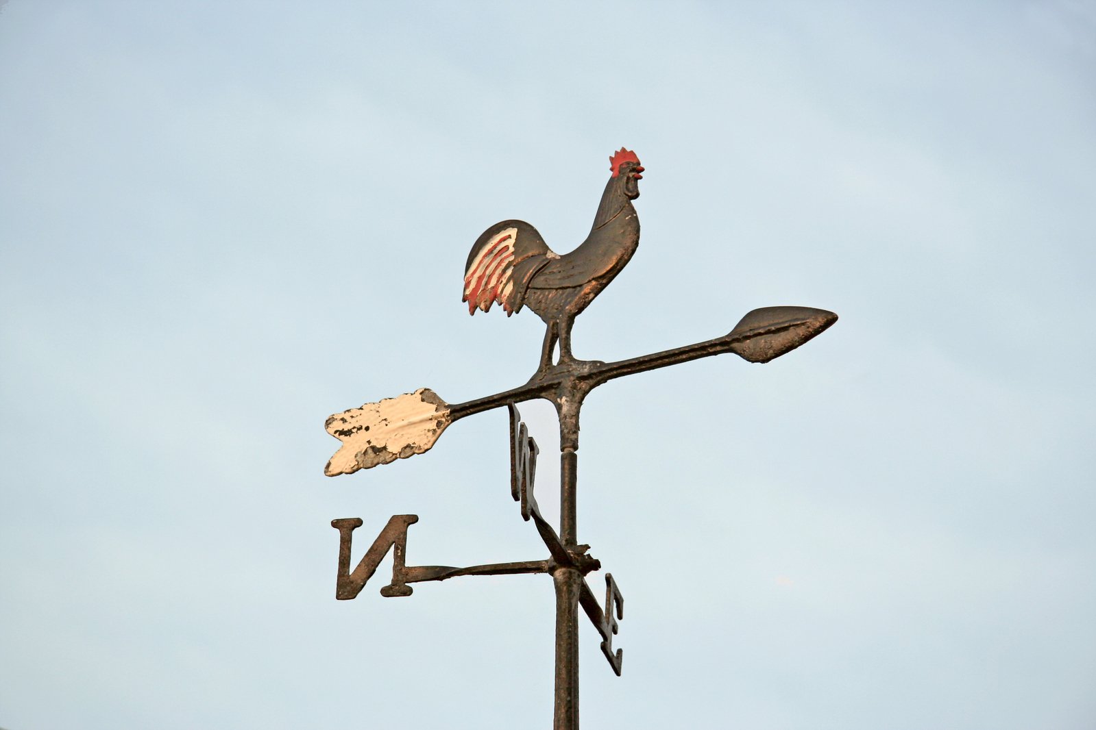 a bird is sitting on top of an old weather vane