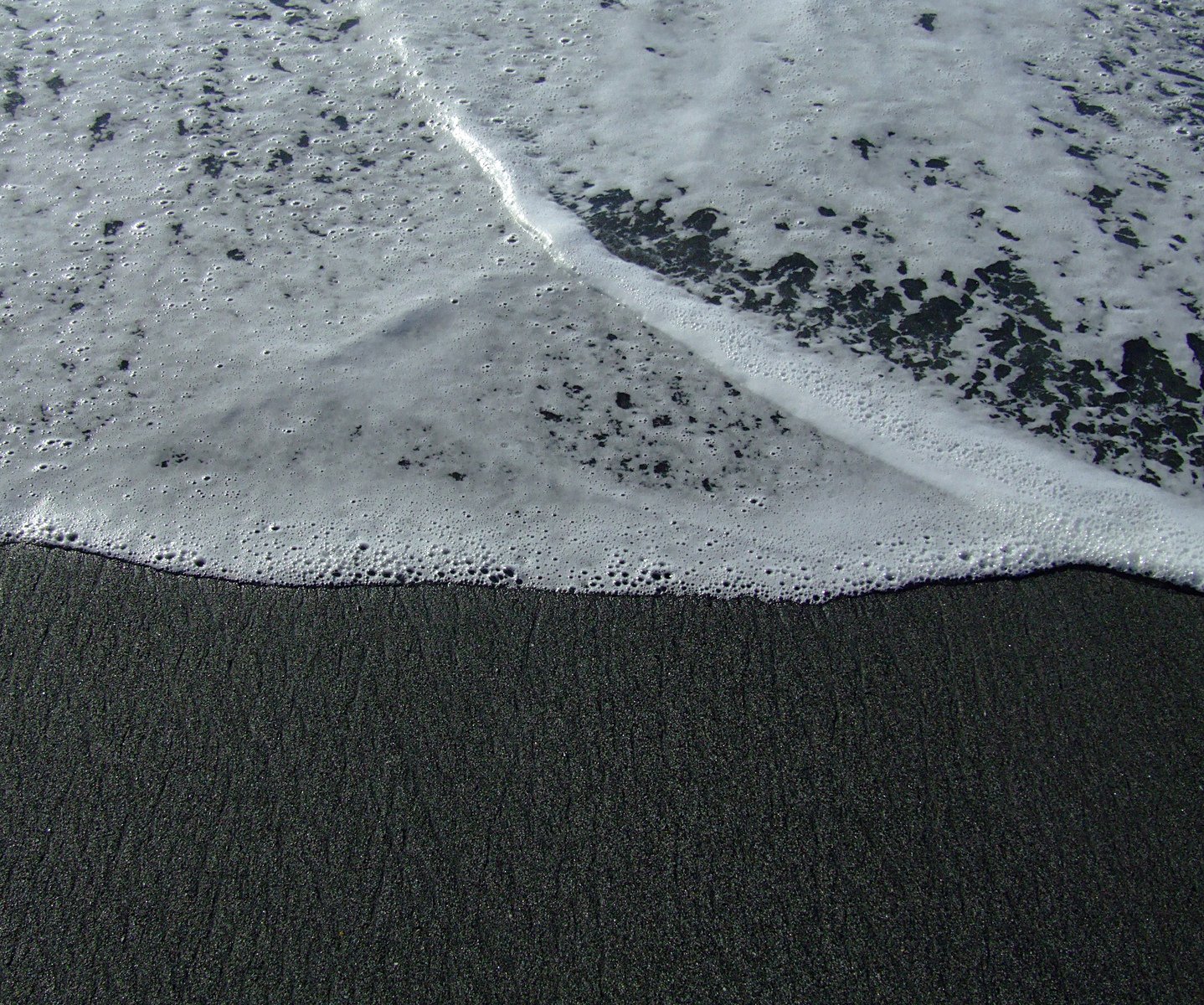 there is a black sand beach with white frothy waves