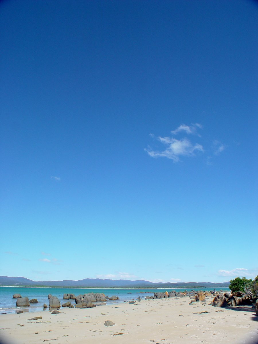 a clear sky above the beach with rocks