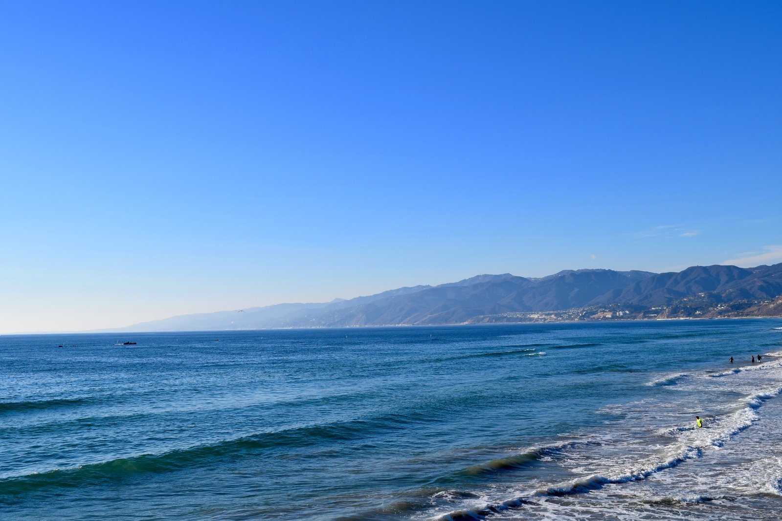 people are on the beach with swimmers in the ocean