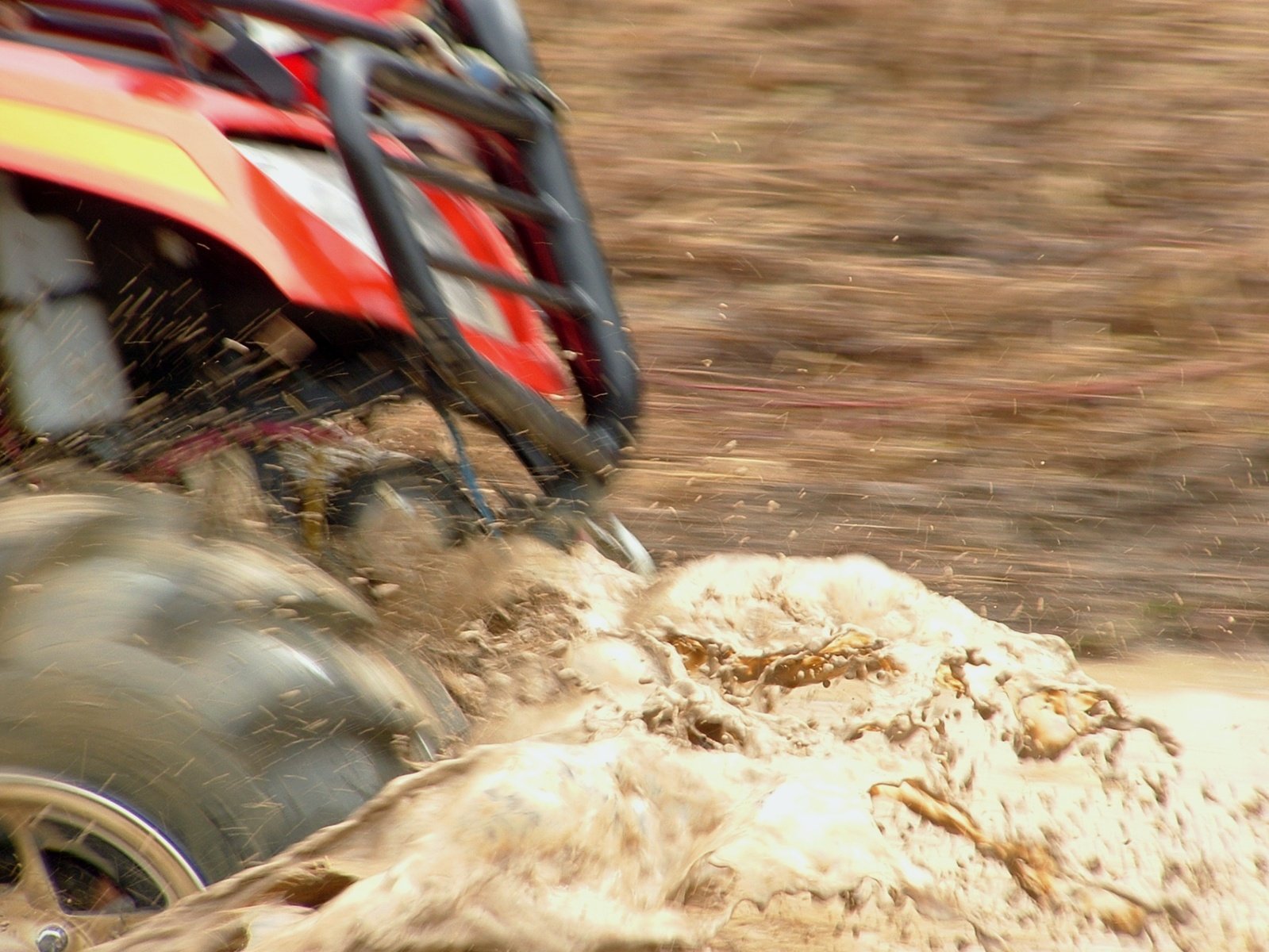 a red four wheeler drives through mud