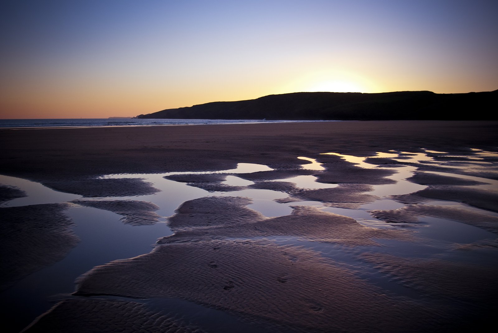 the sun rising behind a small mountain with ocean waves