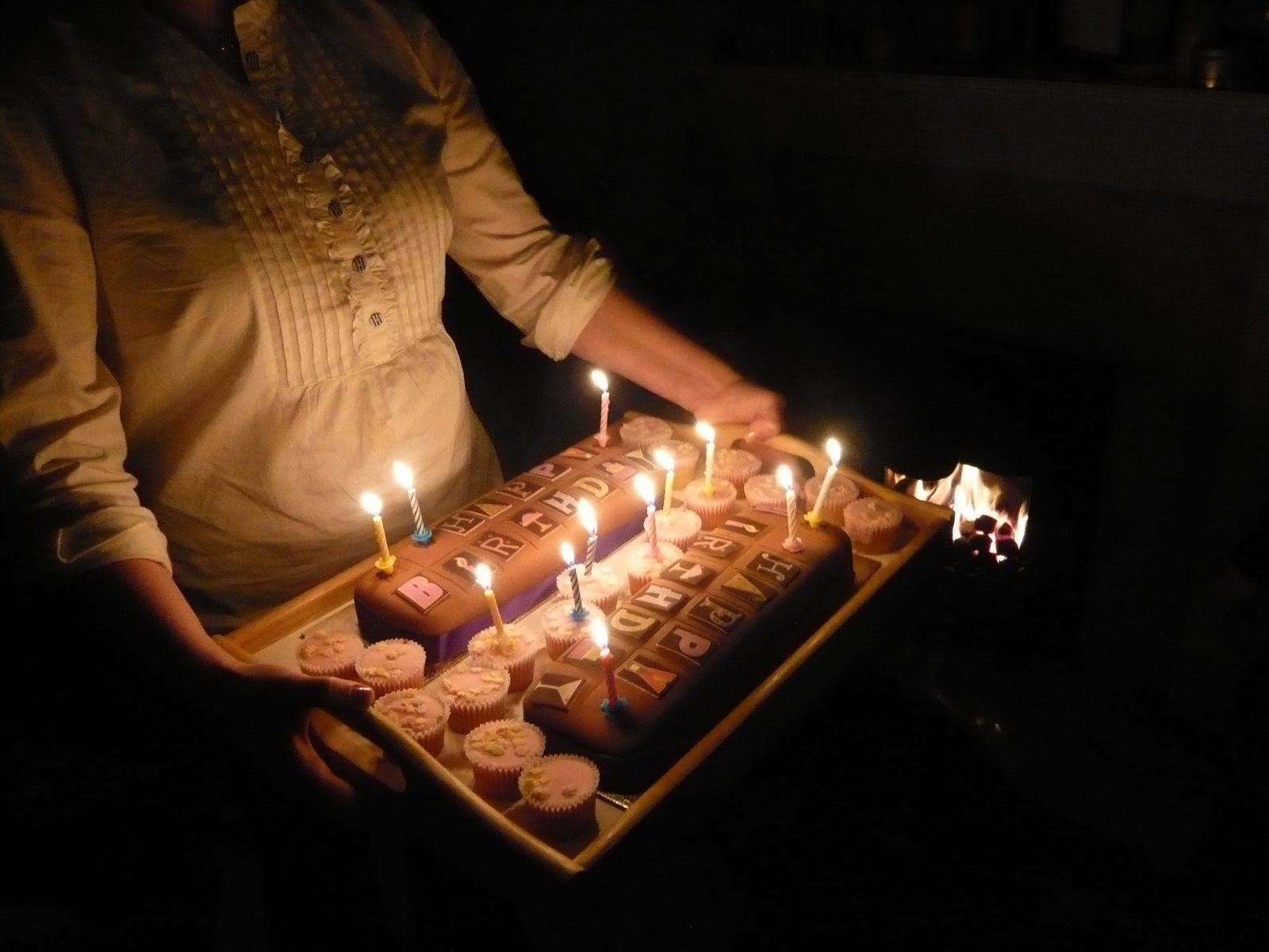 the woman holds a tray with cupcakes with lit candles