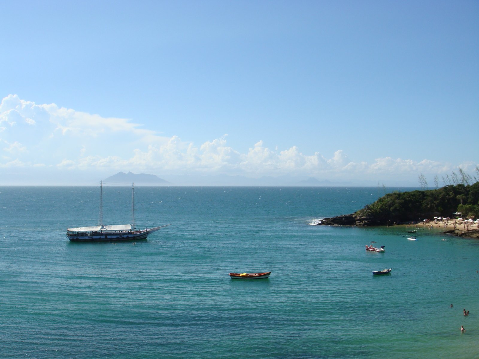 three sailboats out on the water with people on beach in background