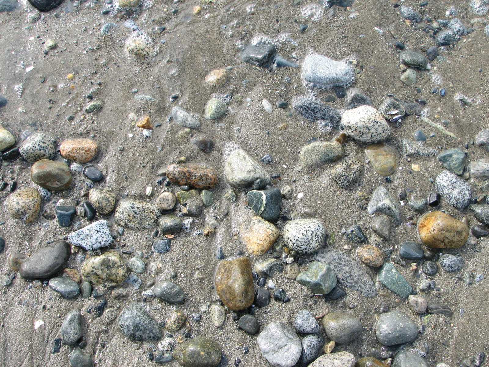 rocks and gravel on the beach and one has an open umbrella