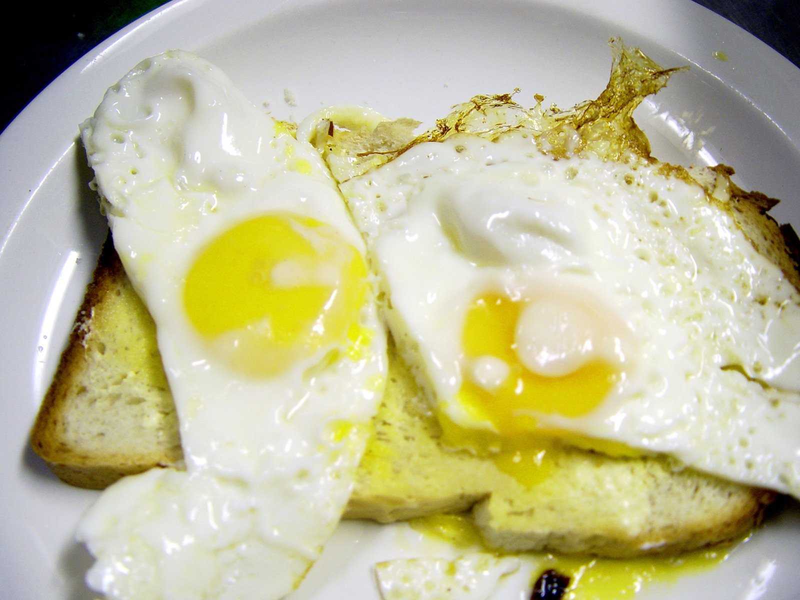 two fried eggs on top of toast sit on a white plate