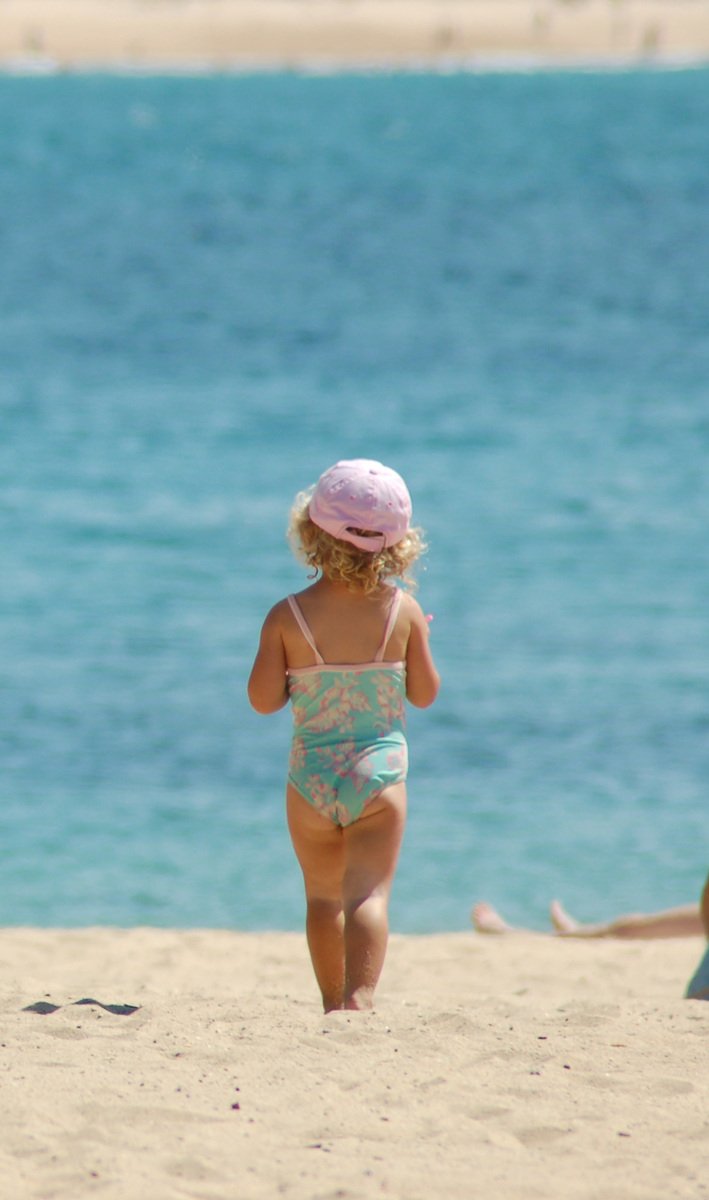 little girl walking on beach in one piece