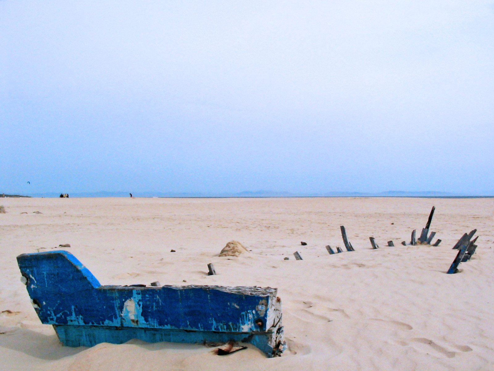 an abandoned blue lounge chair sitting on top of a sandy beach