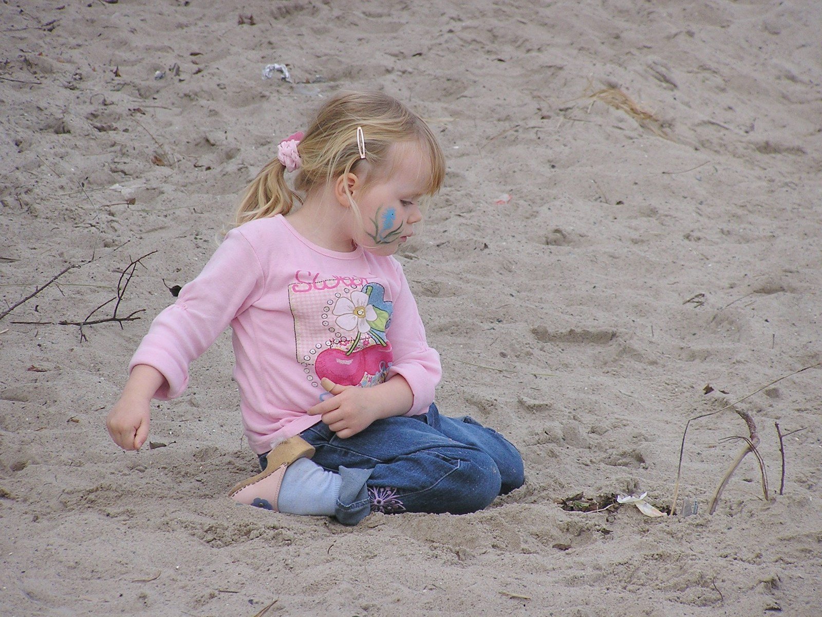 a little girl sitting on the beach with her mouth painted