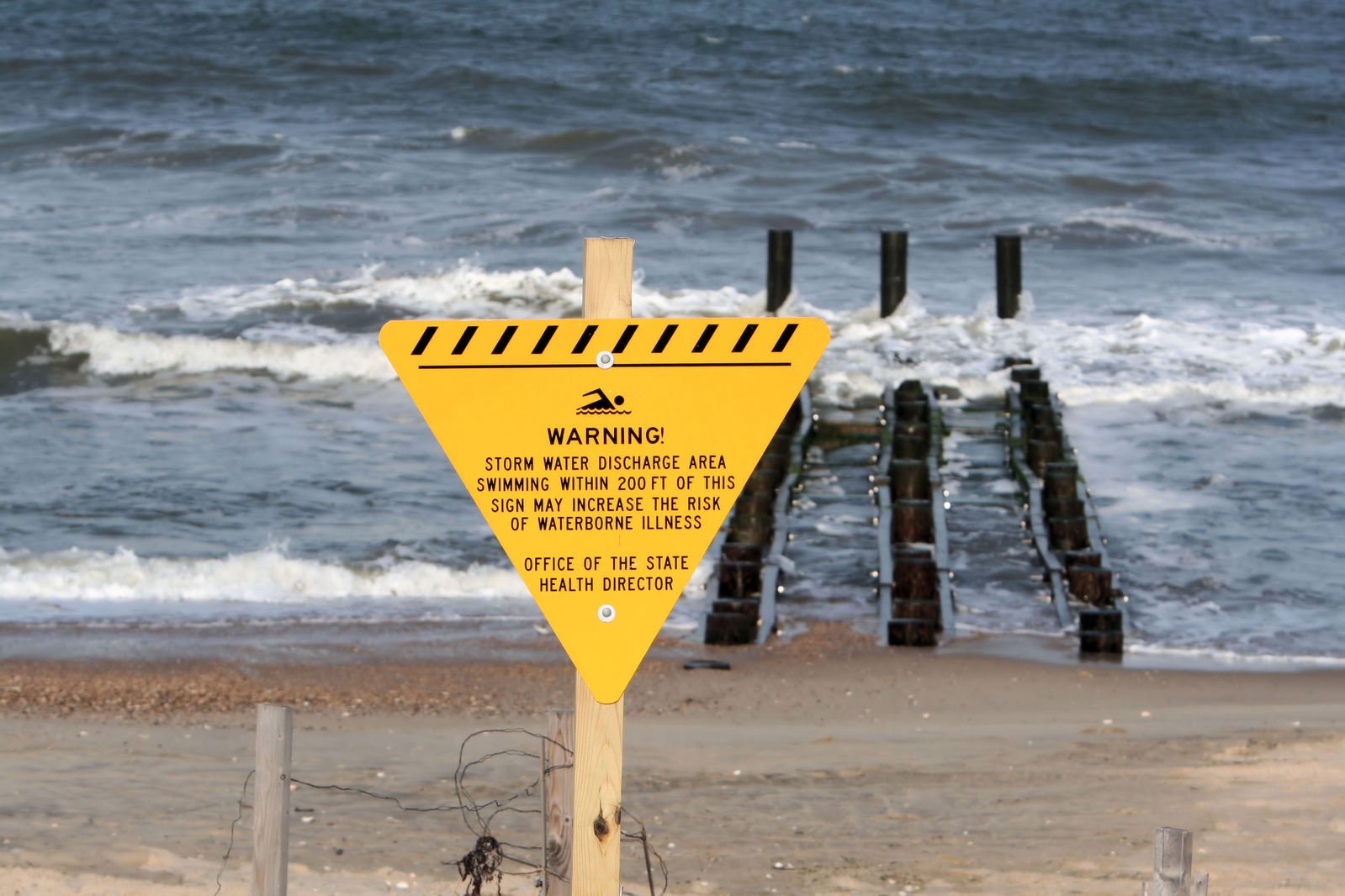 a yellow and black warning sign on a beach