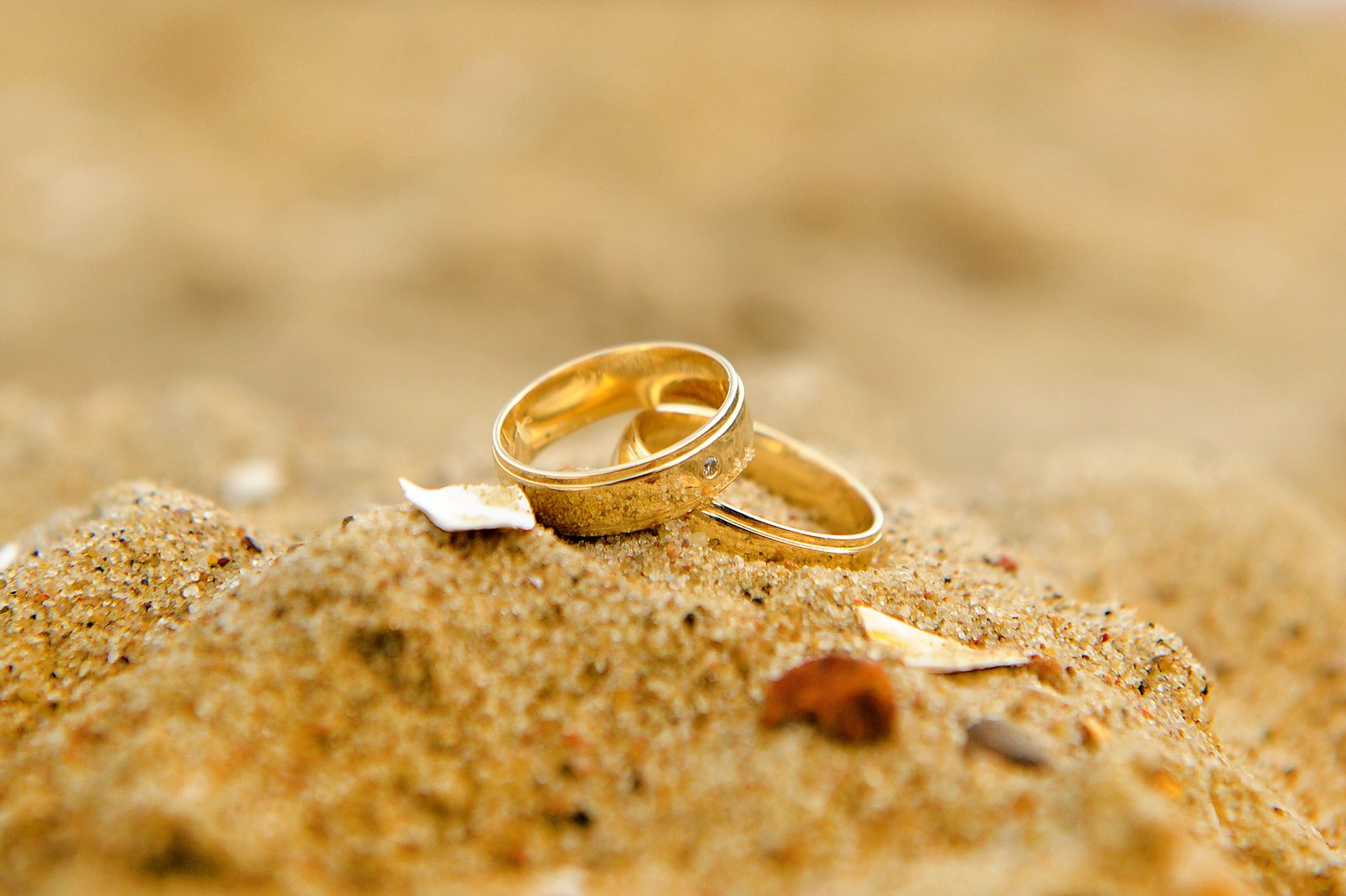 two gold wedding bands that are on top of sand