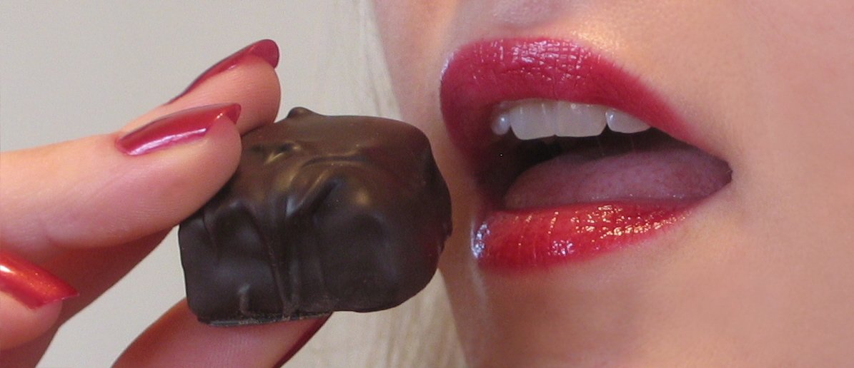 a woman holding up a chocolate piece to her lip