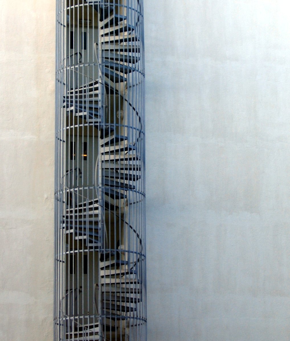 a tall metal sculpture near a building and a wall
