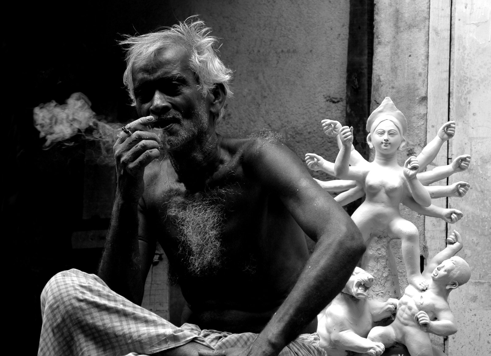 an old man poses for a picture as a small group of statues are behind him