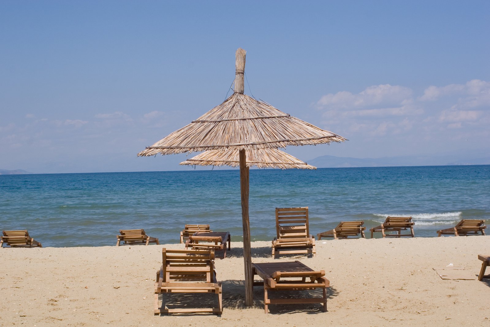 a wooden beach umbrella next to lounge chairs