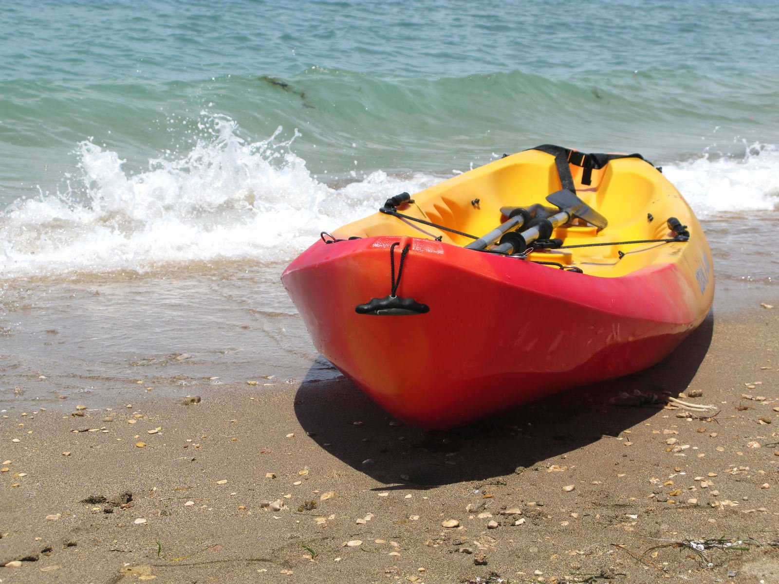 a kayak resting on the beach with a life vest tied to it