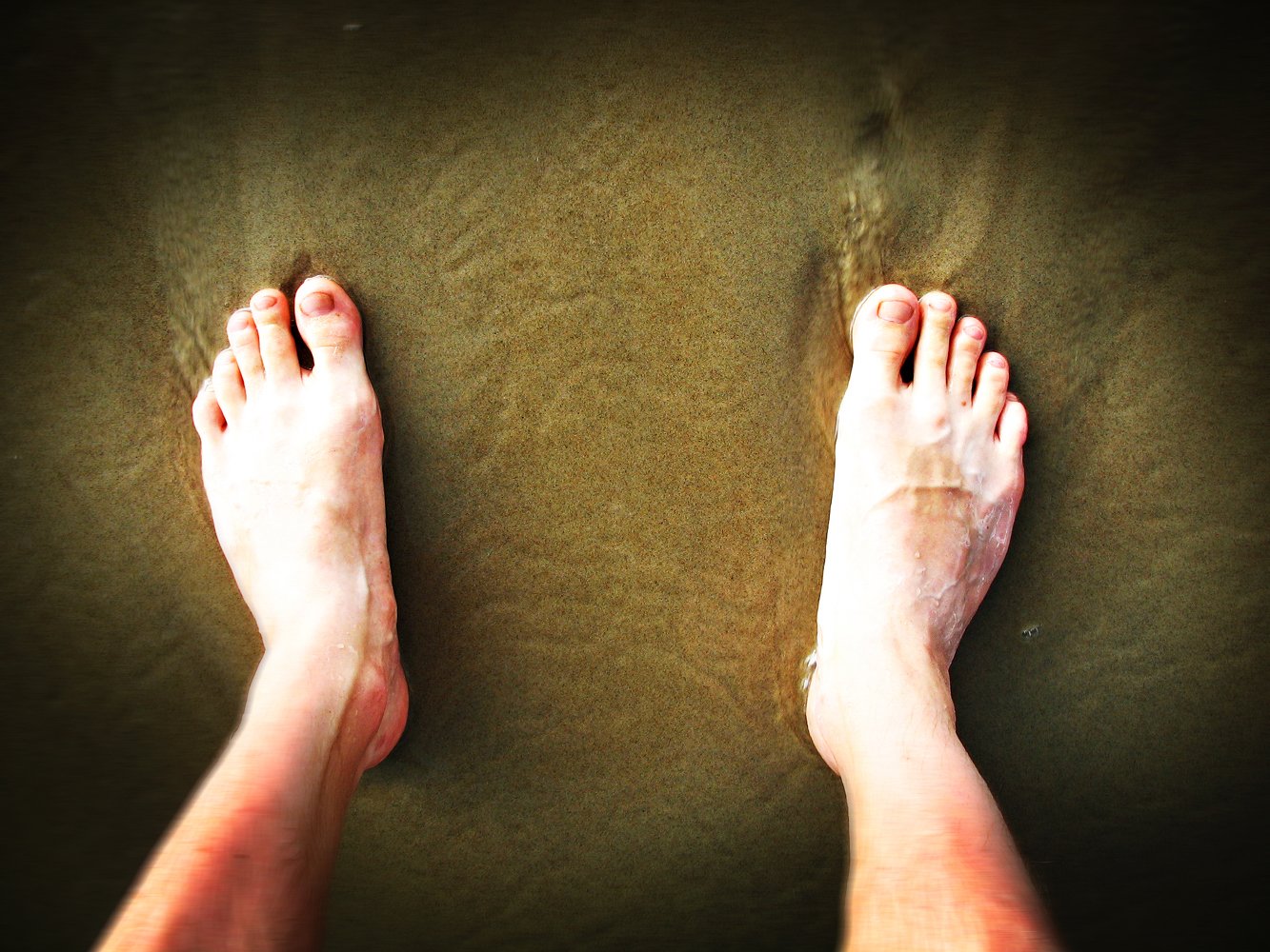 the bottom of two bare feet standing on the sand