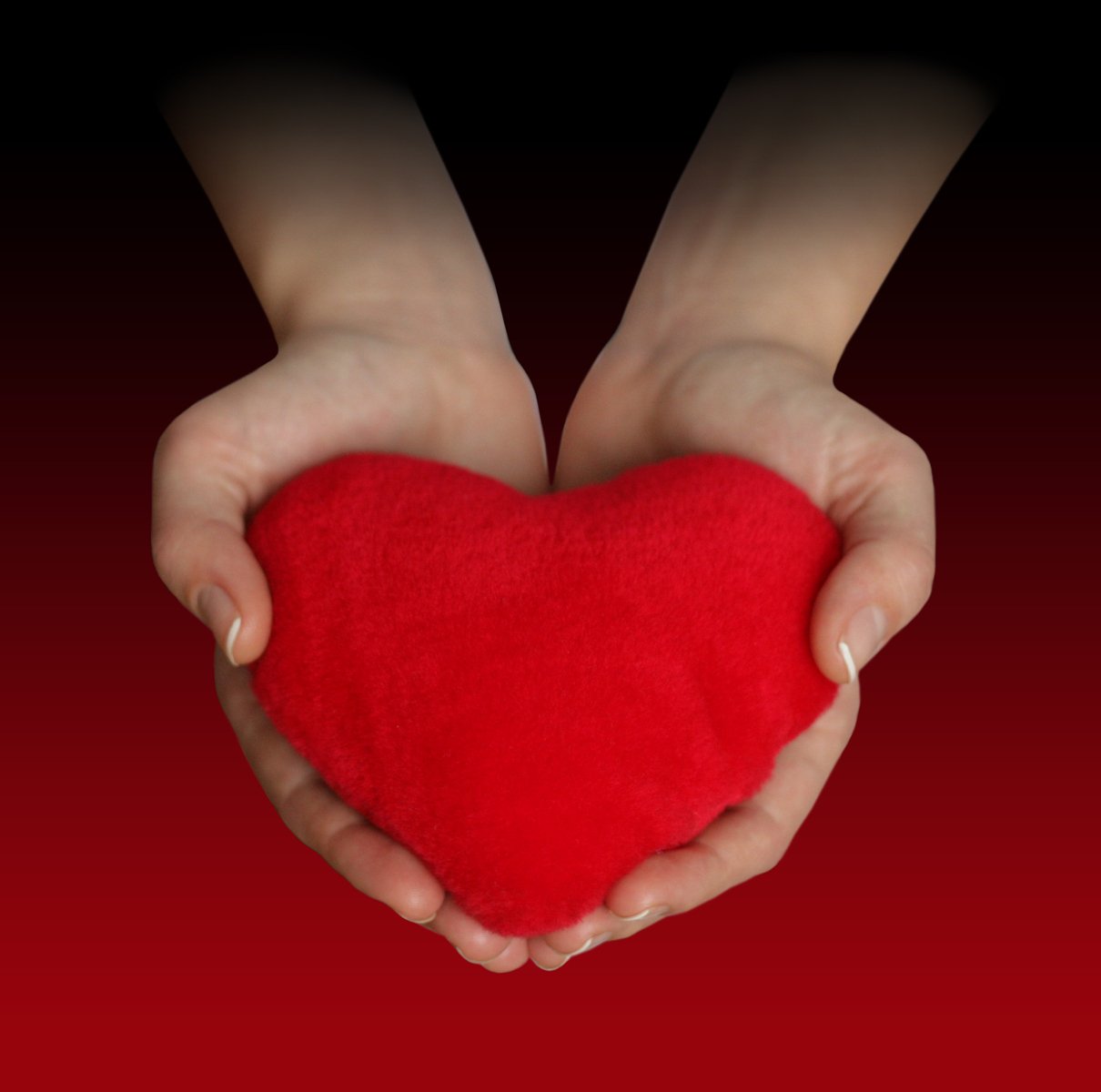 hands are holding a heart shape pillow over a red backdrop