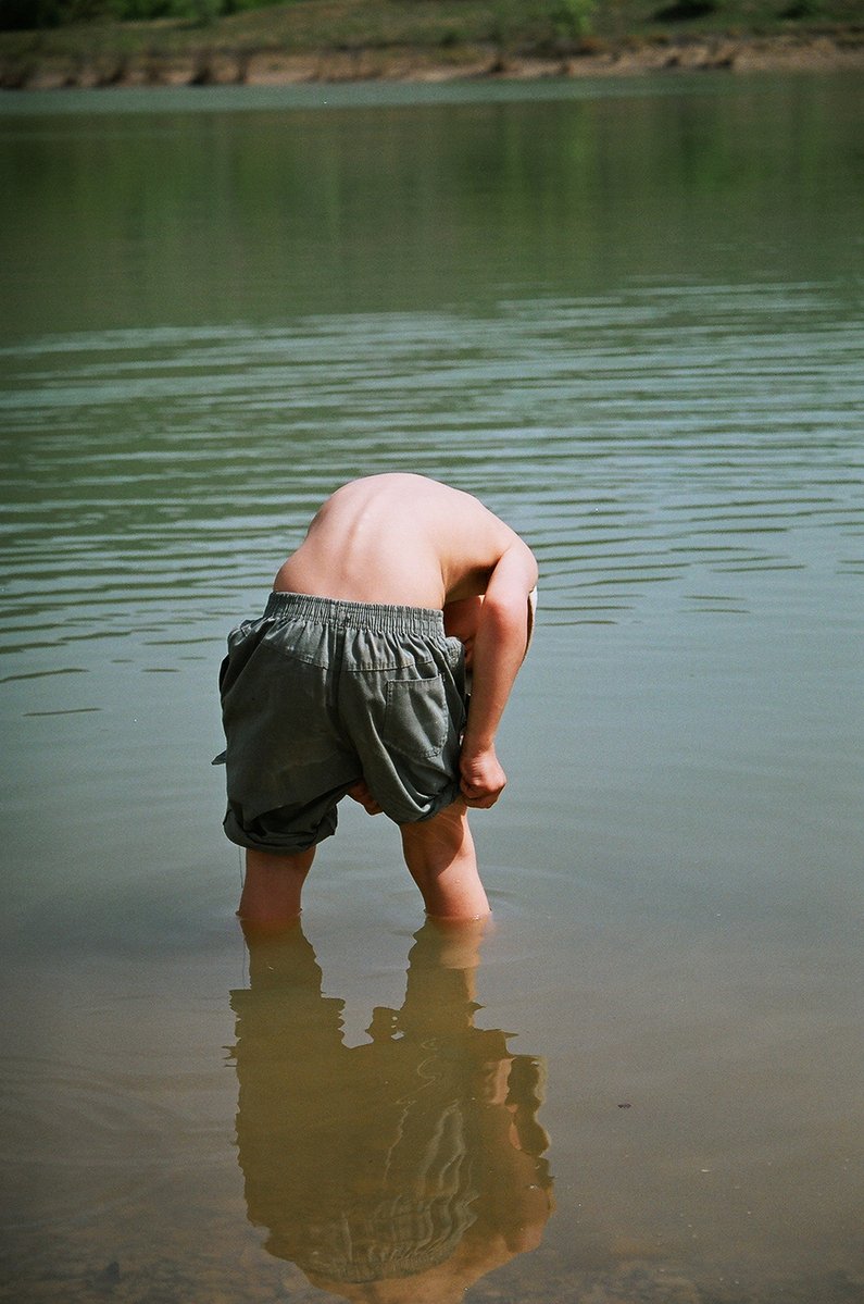 a person bent over in shallow water looking at soing