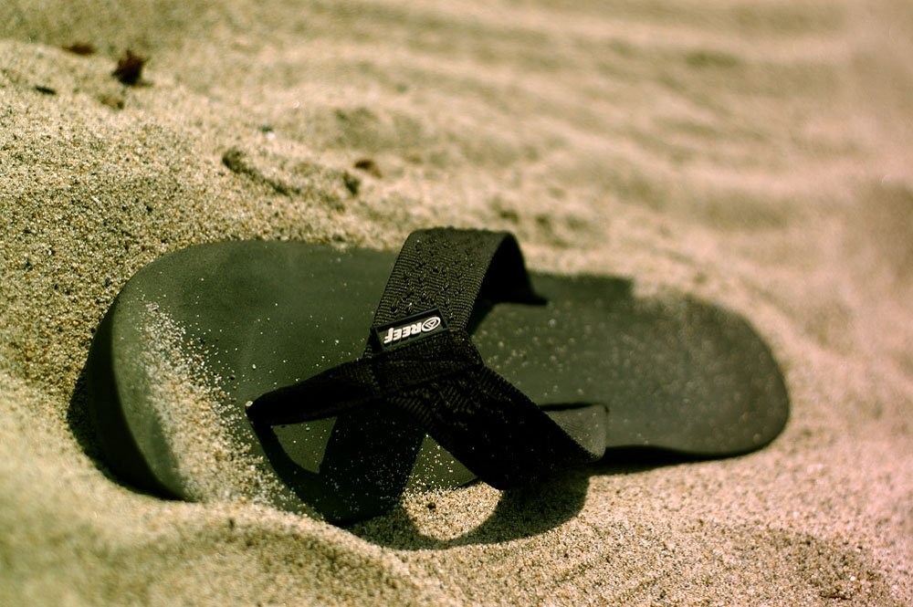 a pair of black flip flops lays in the sand