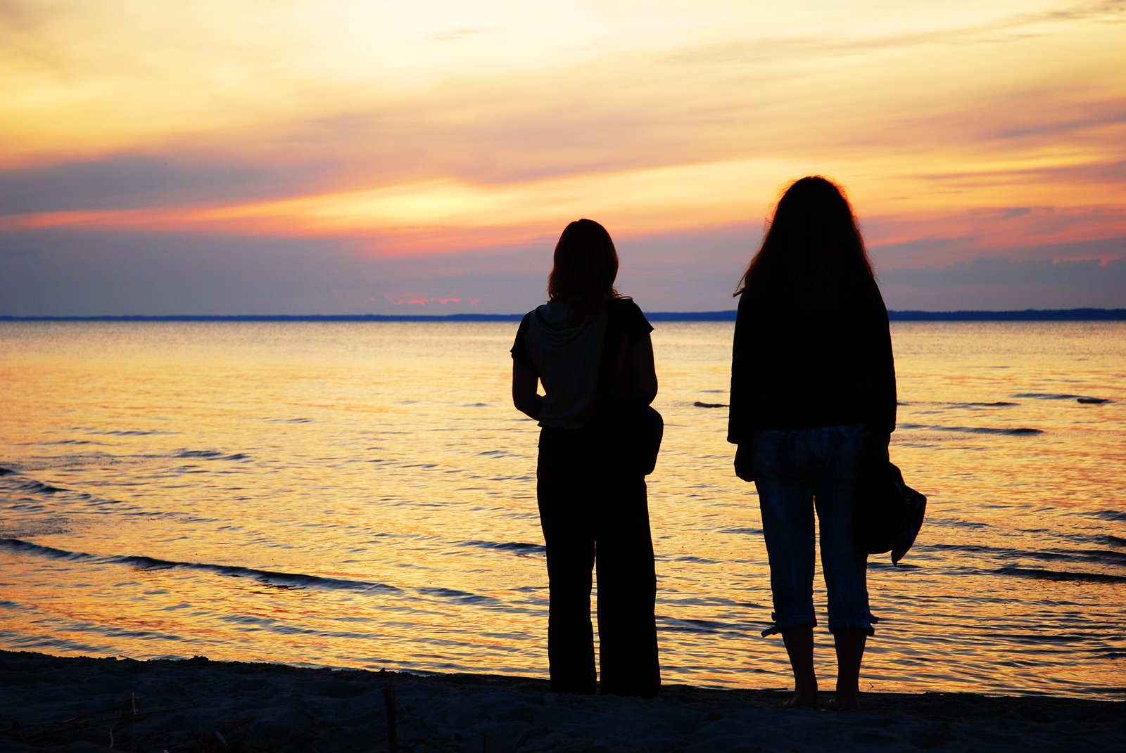 two people standing on the sand watching the sun rise