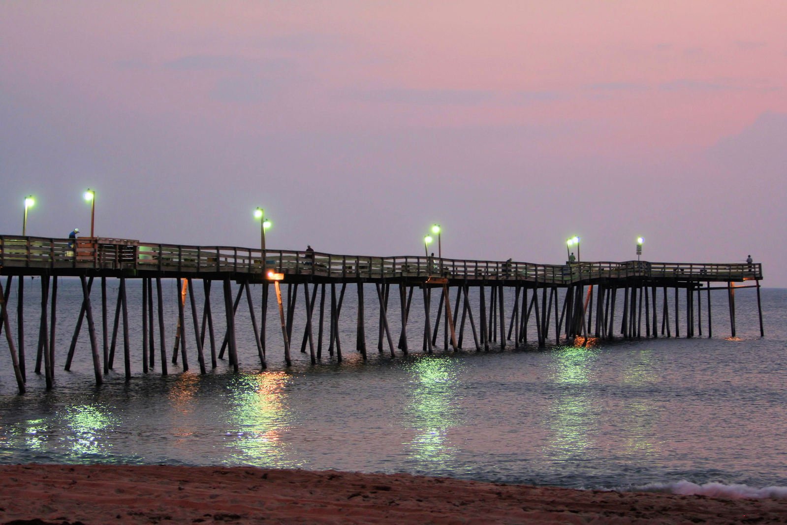 pier illuminated at dusk at the ocean with people walking on it