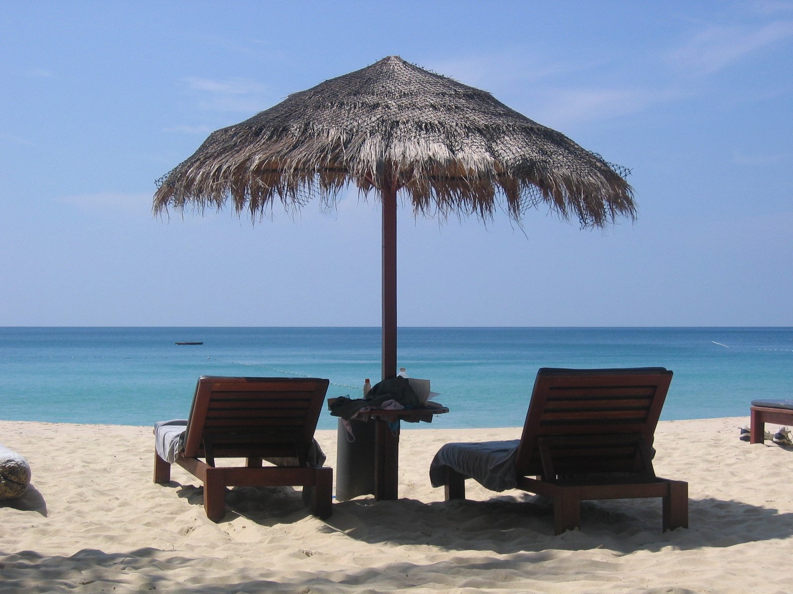 two brown wooden chairs and an umbrella on a beach