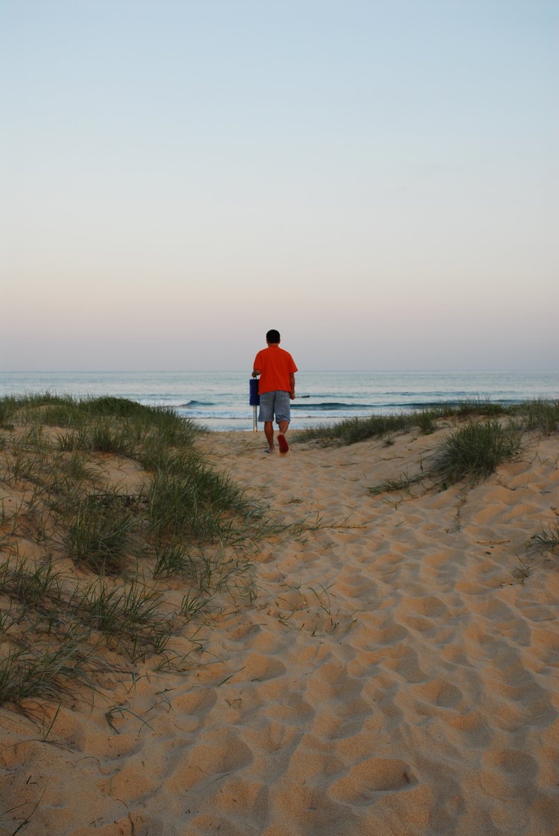 a man in an orange shirt and shorts walks on a sandy beach towards the ocean