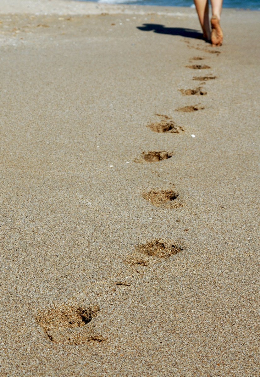 a woman walking down a beach with a long trail