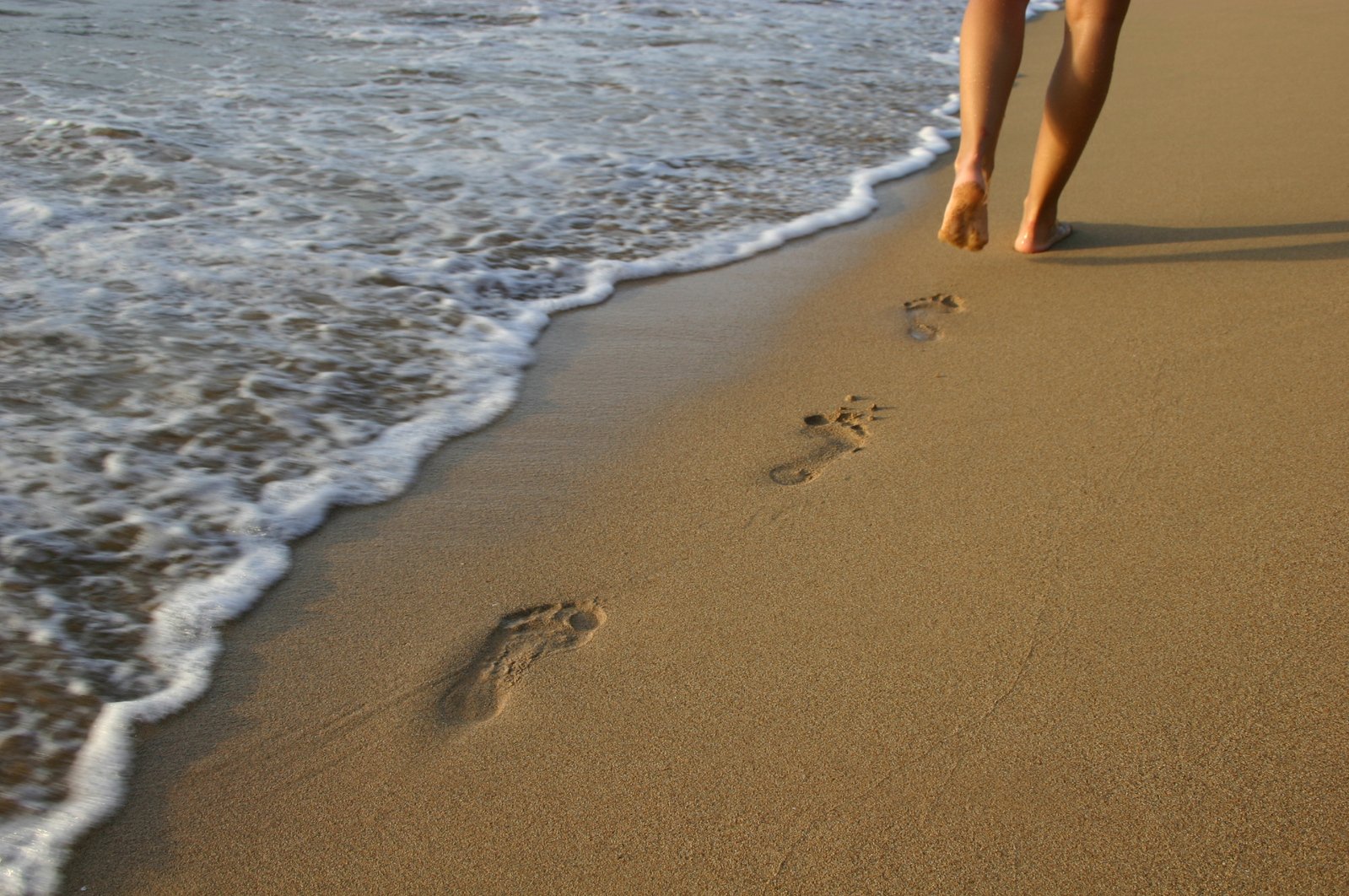 a barefoot person walking on the beach next to an ocean