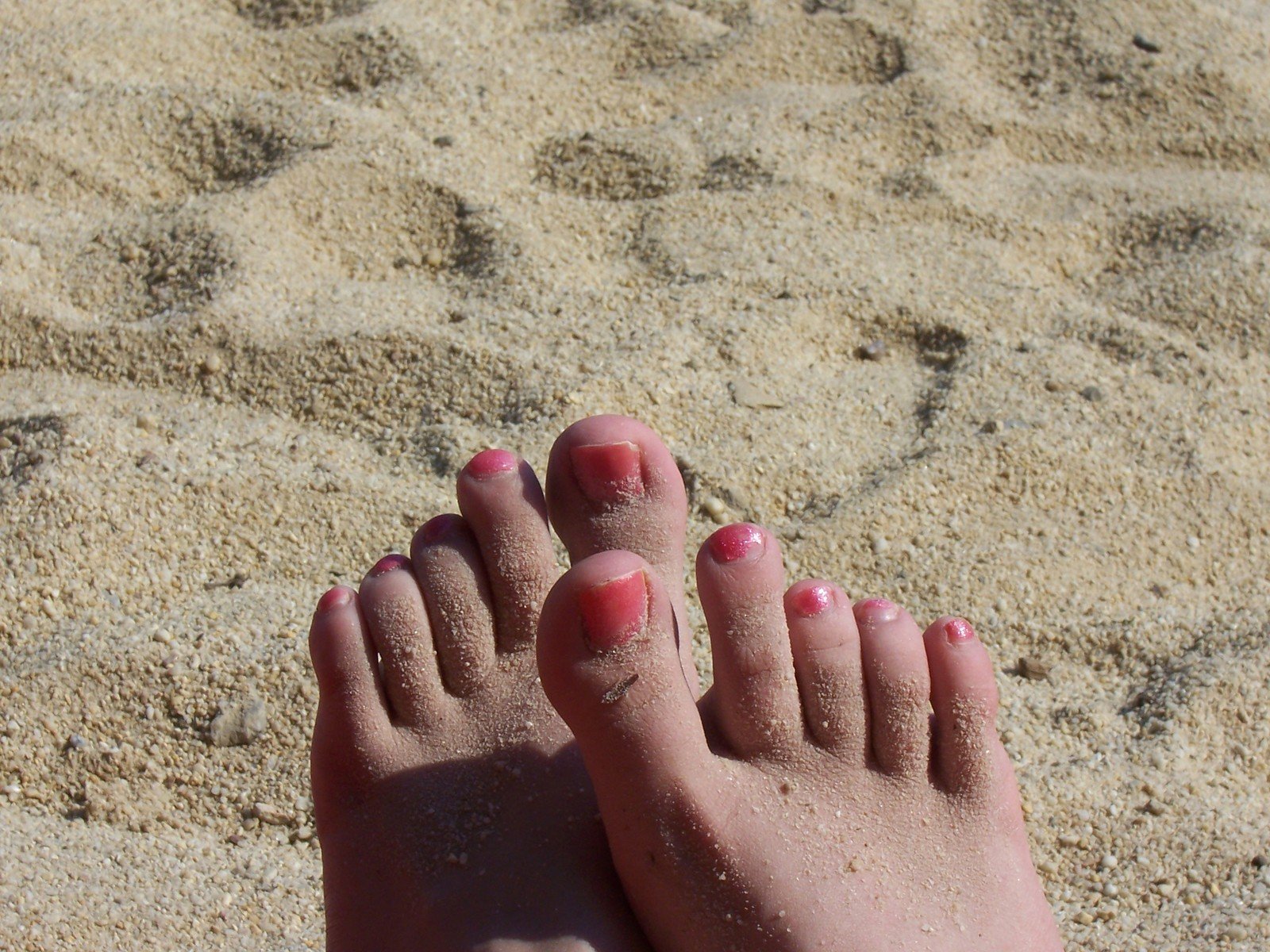 two feet in sand at a beach with pink toenails