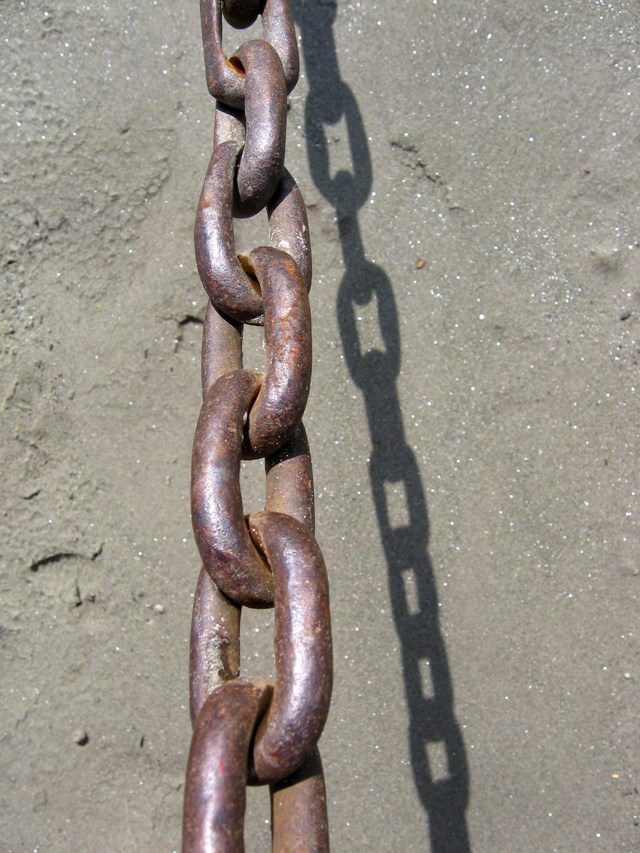 a very long rusty chain with links next to a curb