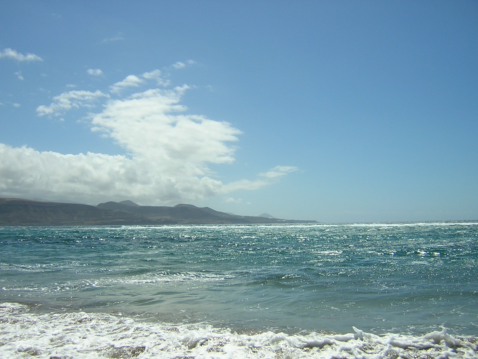 the water at the beach is calm with mountains in the distance