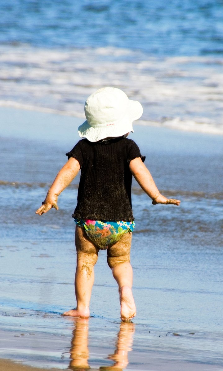 a small child in shorts and a hat at the beach