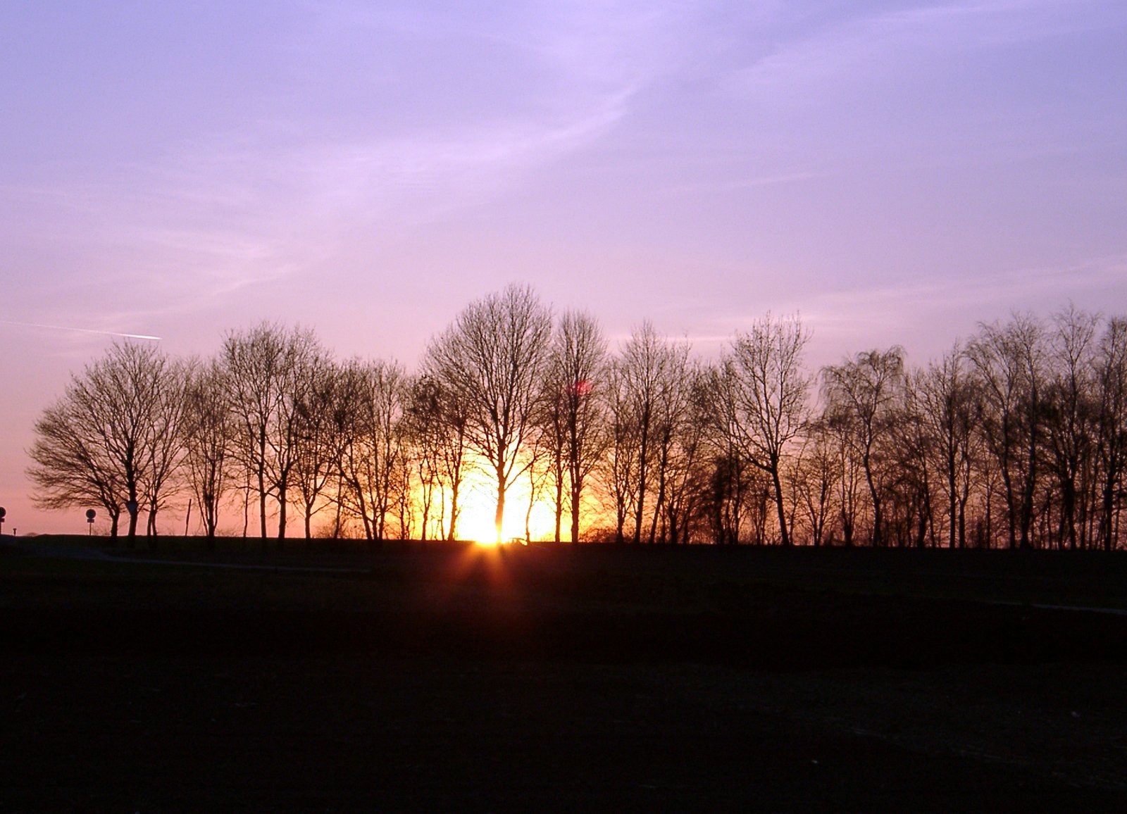the sun is setting in the distance over some trees
