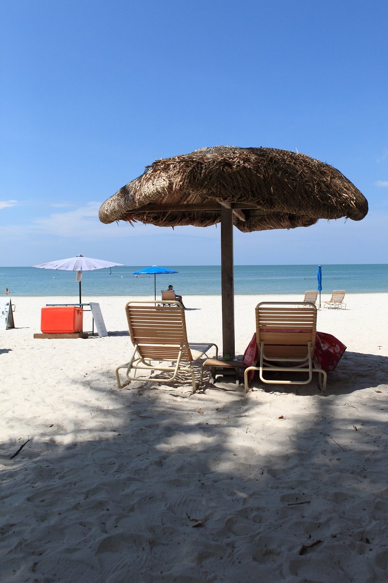 two lounge chairs under an umbrella on the beach