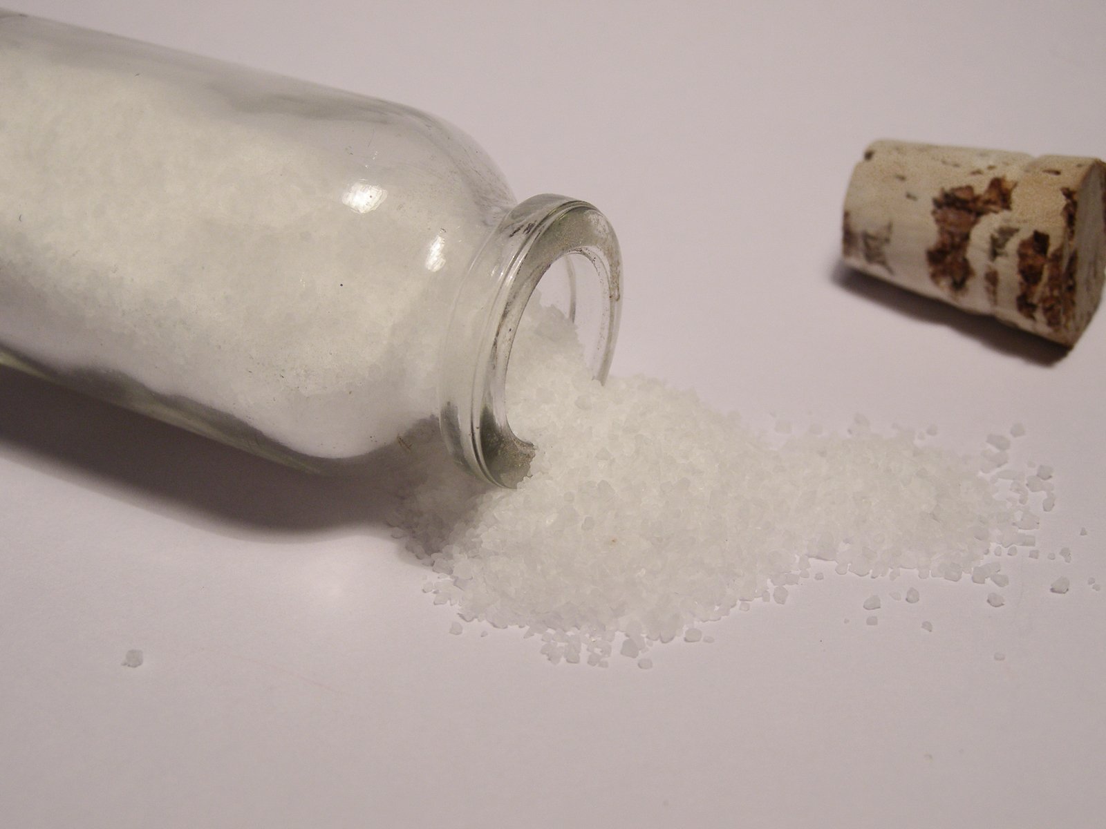 a pile of rice spilled into a bottle next to a cork lid