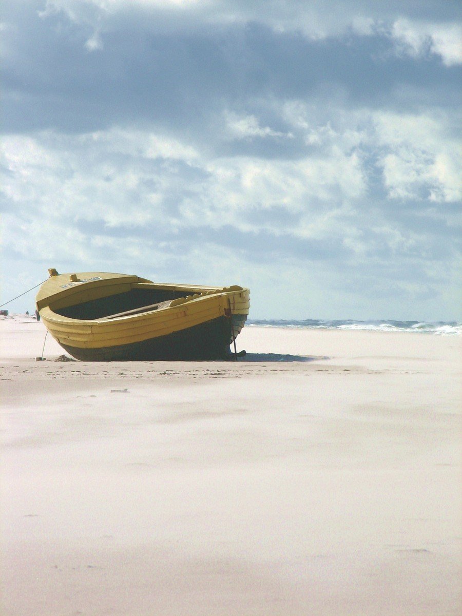 a lone boat sits on a sandy beach