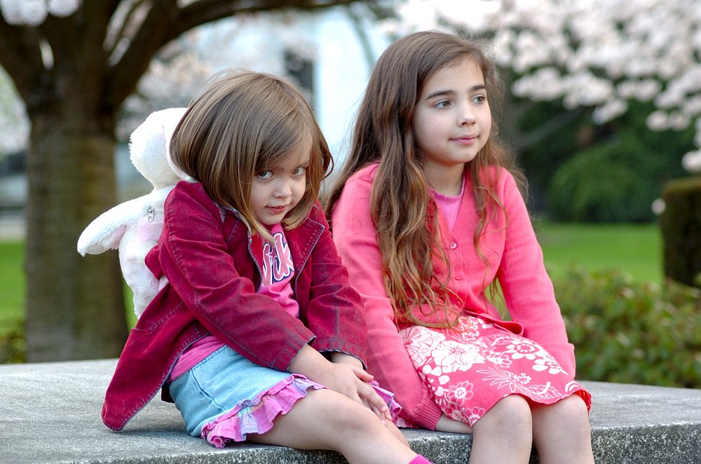 two girls sitting on cement wall with trees in background