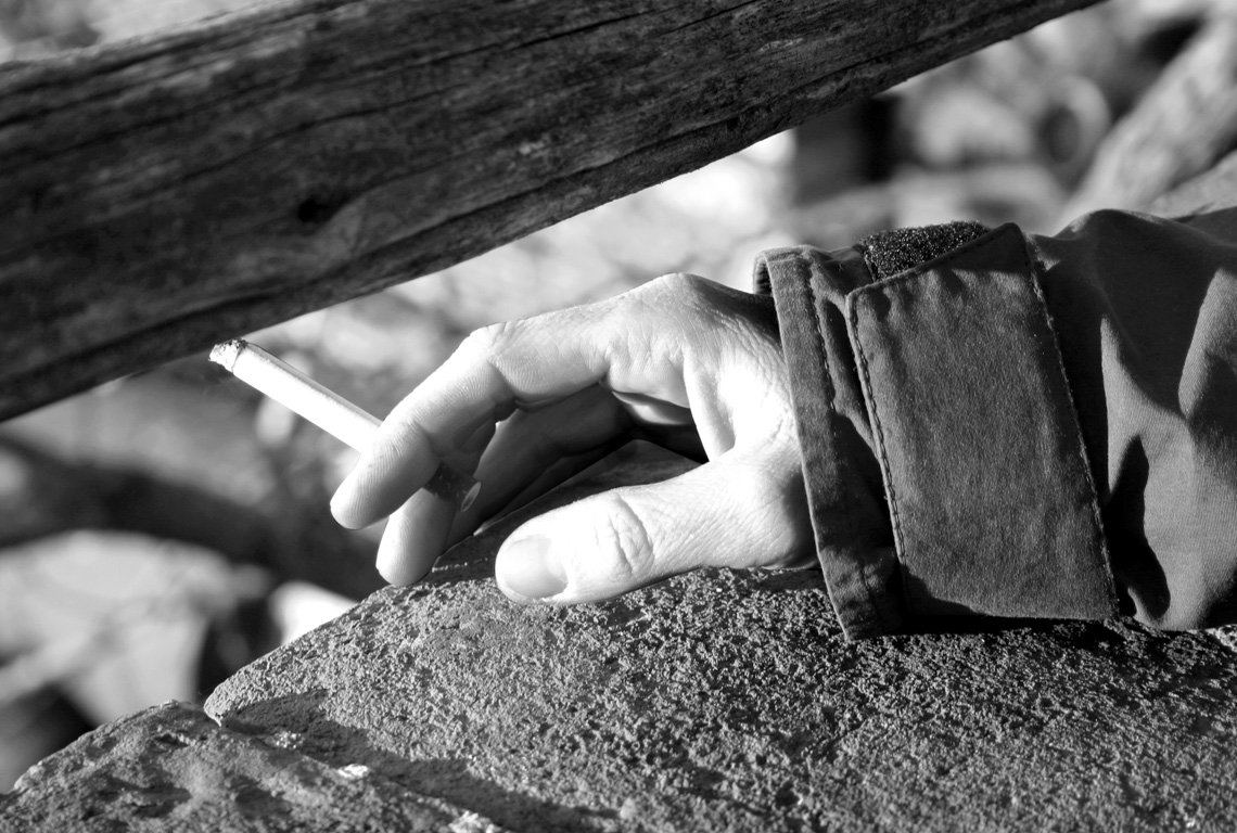 a person is holding a cigarette while leaning against a fence