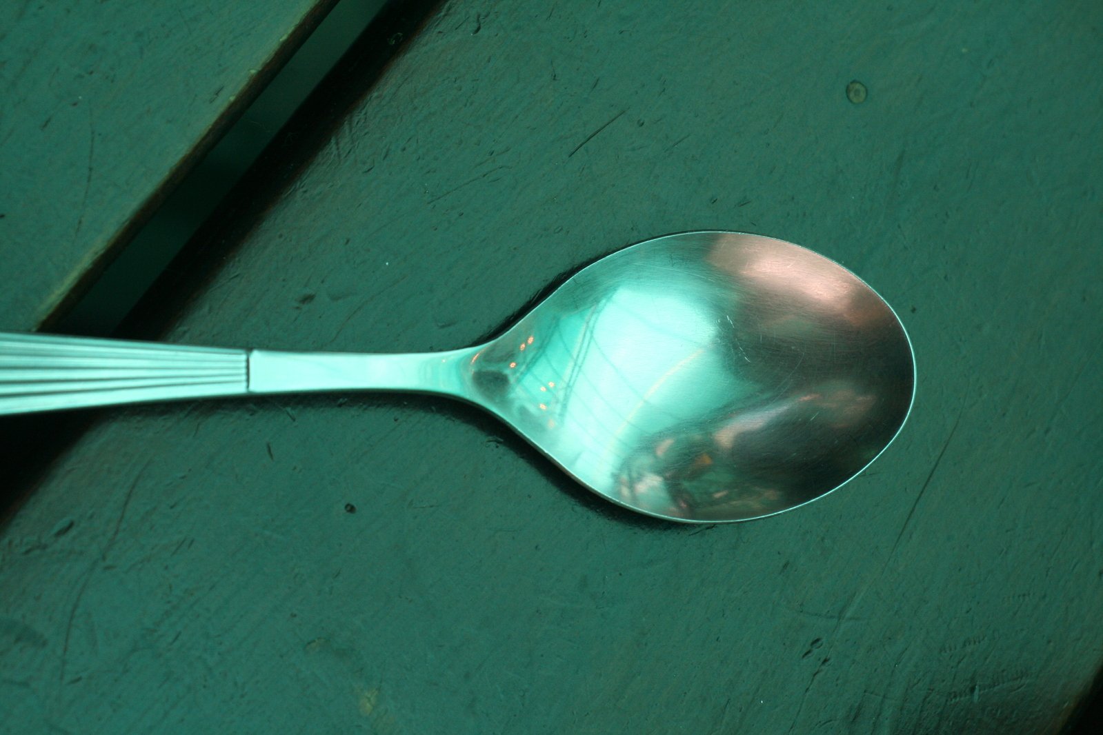 the silver spoon sits on a green wooden surface