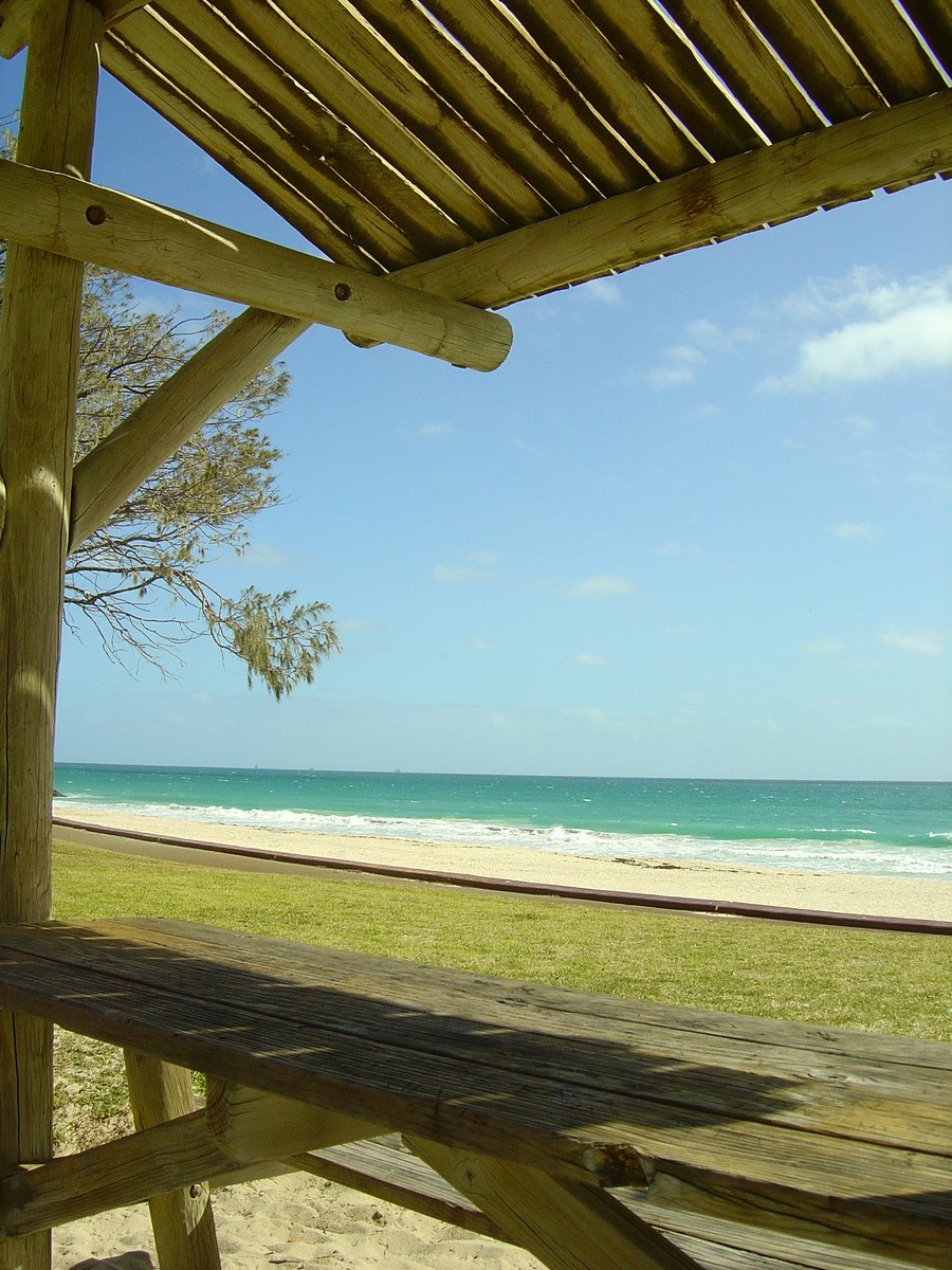 a wooden bench is on the beach by the ocean