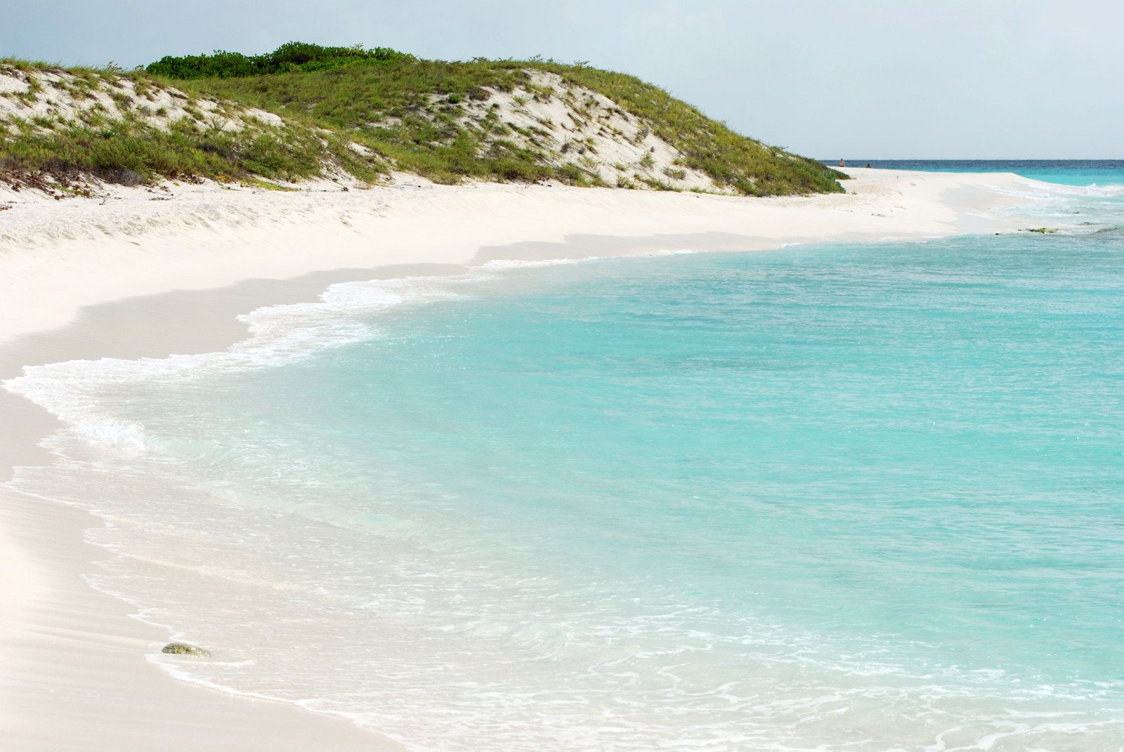 a sandy beach with turquoise water and a green hill in the distance