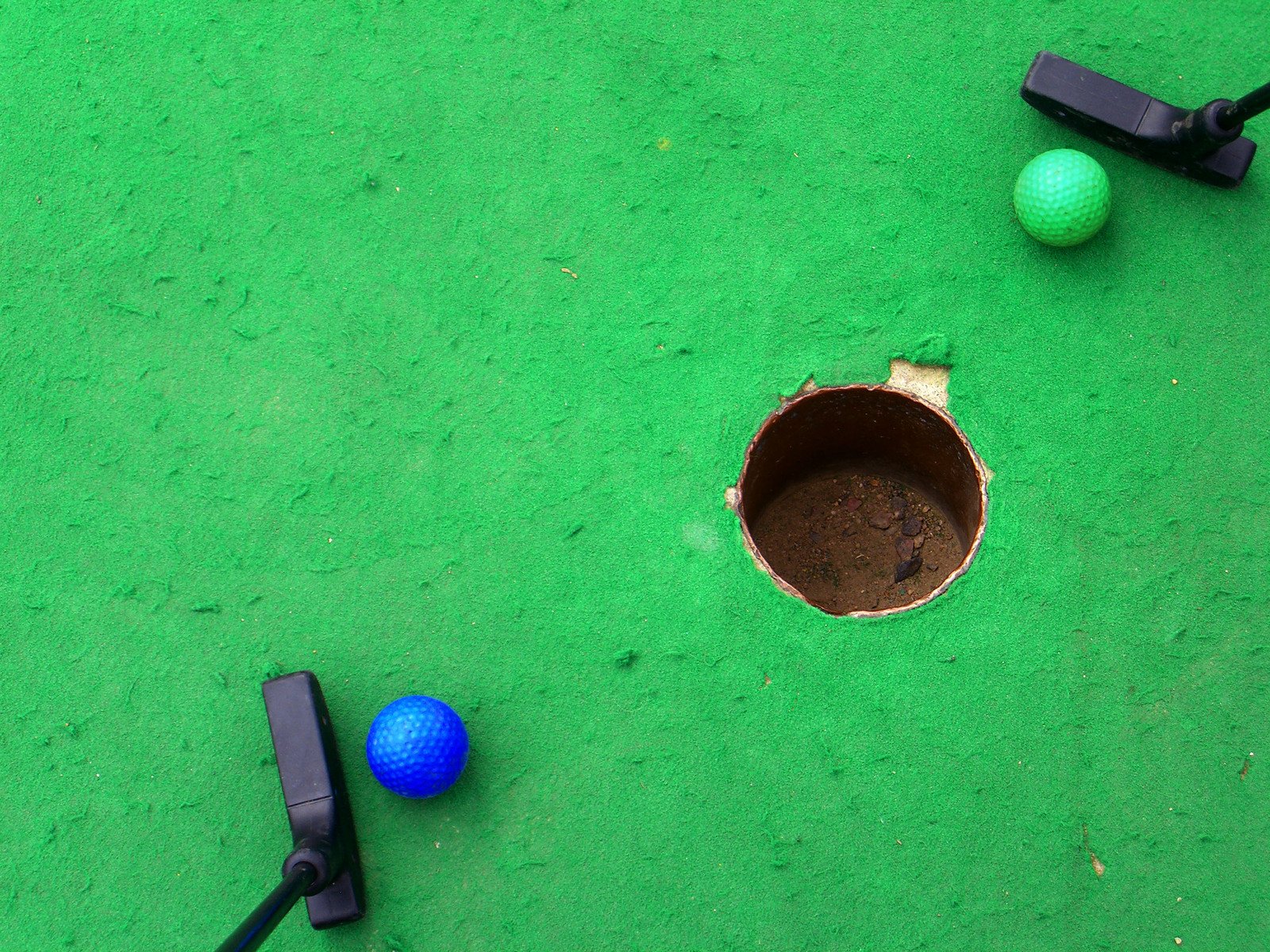two golf balls next to a hole in the green ground
