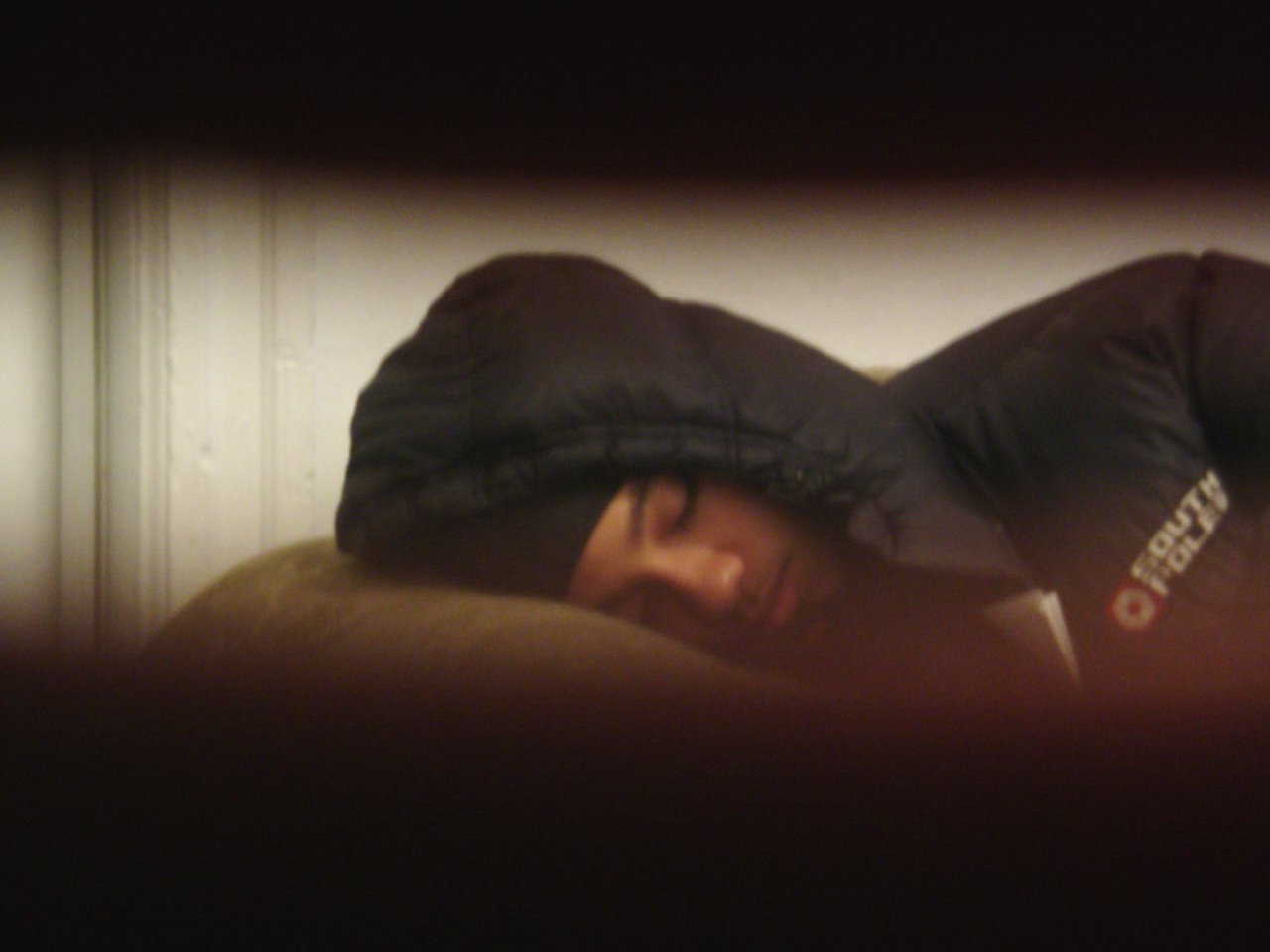 a man in black hoody laying down with his head covered by pillows
