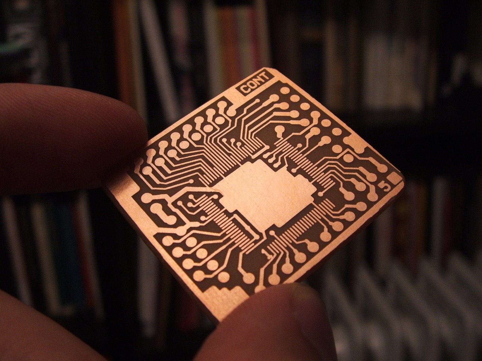 a hand holds up a wooden circuit board that has been engraved onto it